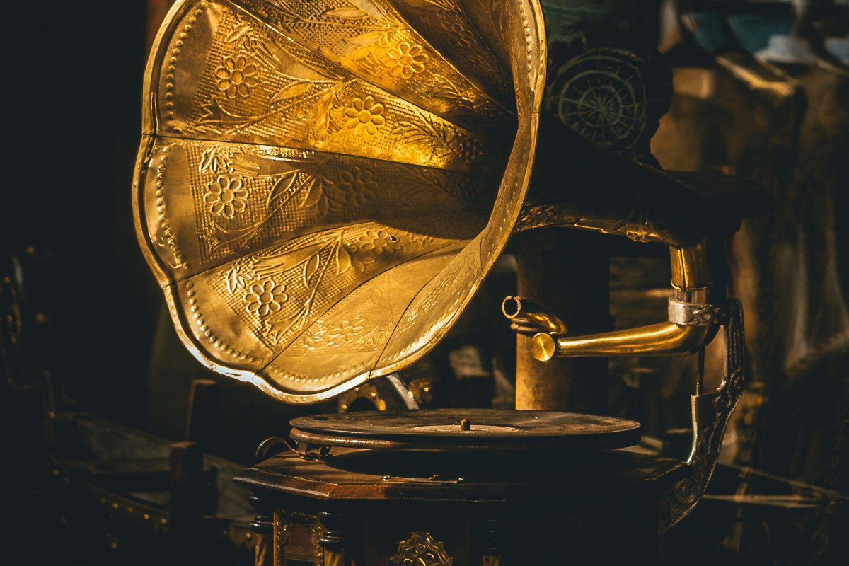 A vintage gramophone with an intricately engraved golden horn, reflecting warm light in a dimly lit setting, evoking a nostalgic atmosphere.