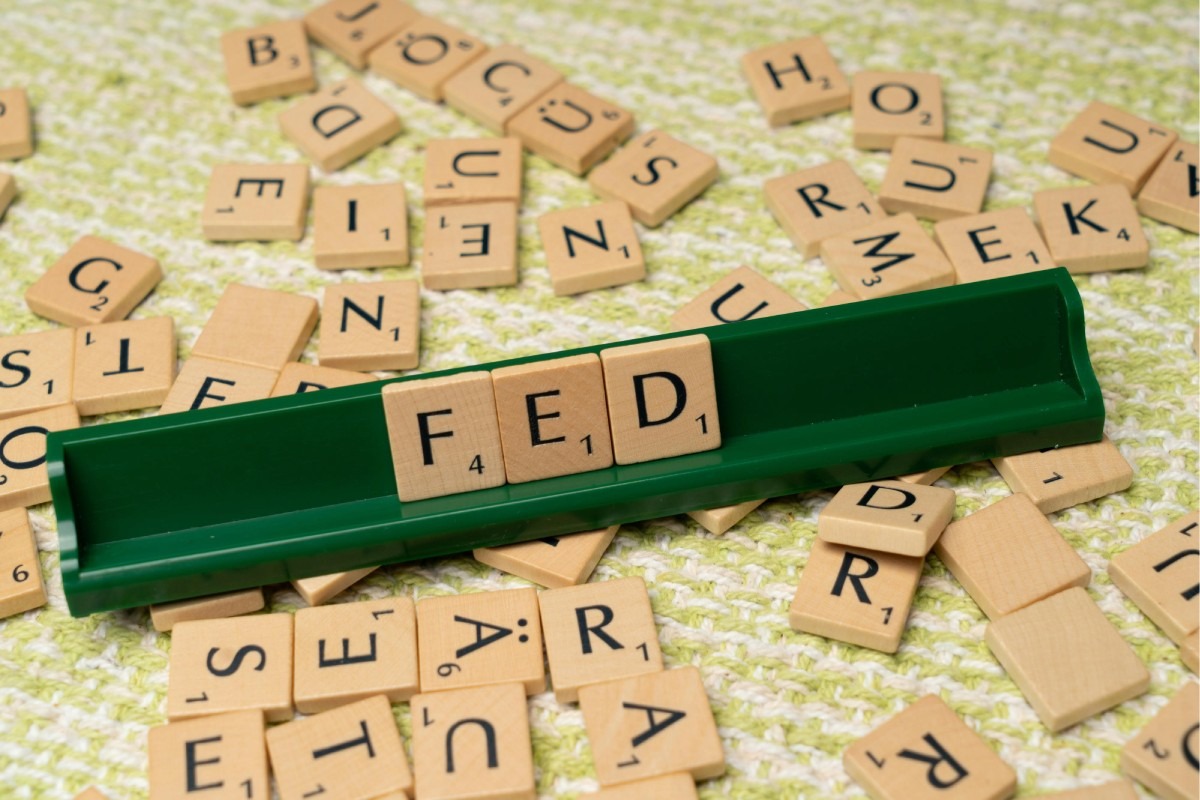 Wooden letter tiles scattered on a surface, with the word 'FED' arranged on a green tile rack in the centre.