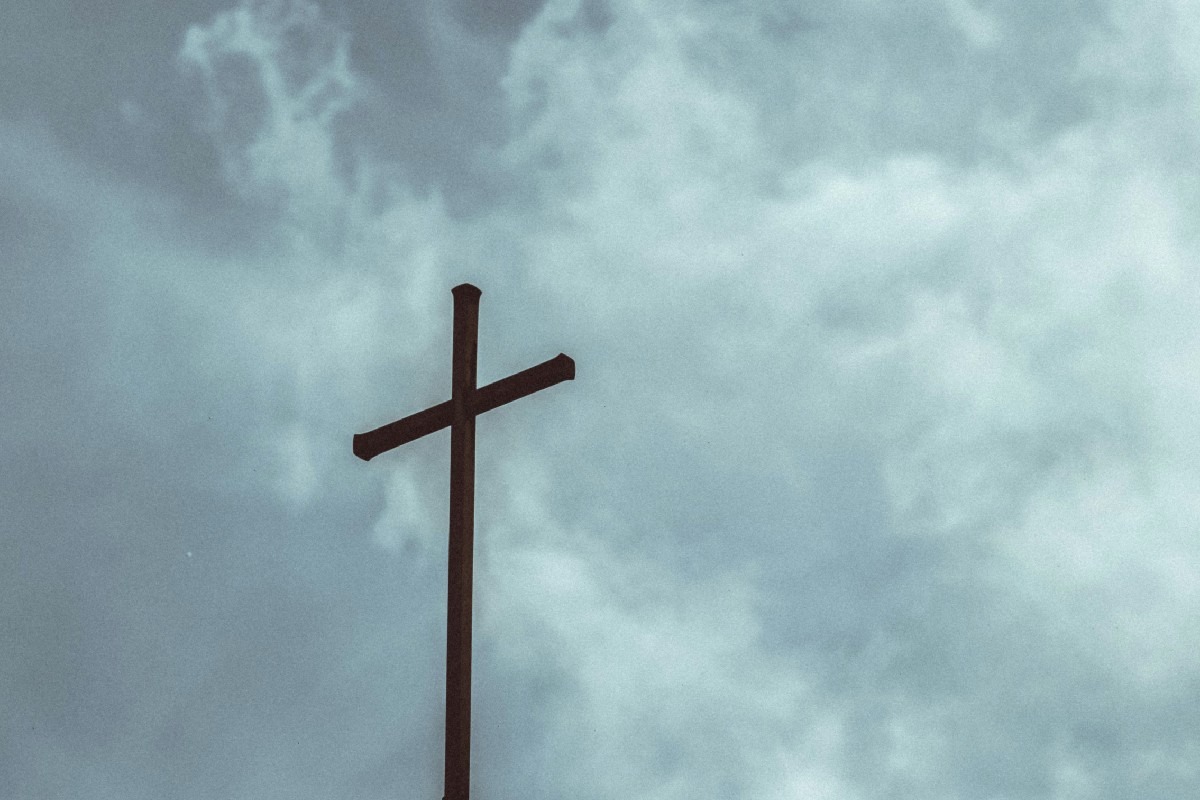 A wooden cross silhouetted against a cloudy sky.