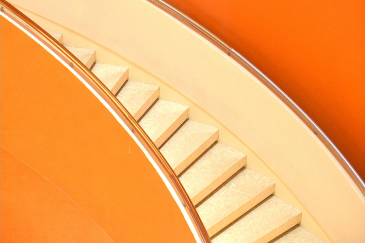 A curved staircase with white marble steps and orange walls, featuring sleek metal railings, creating a modern architectural composition.