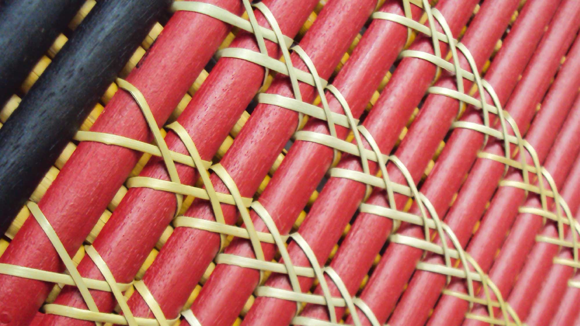 A close-up image of interwoven red and black rods tied with thin strands, creating a geometric pattern that represents structure and connection.
